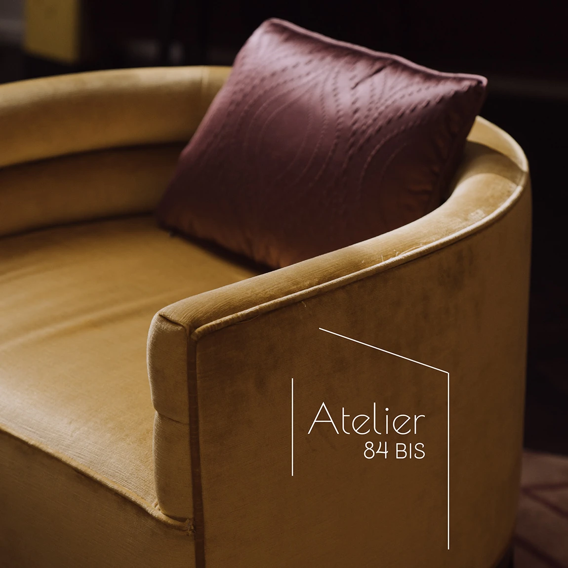 Logo blanc de l’Atelier 84 bis sur un fauteuil en velours ocre et son coussin prune, planche de l’identité de marque