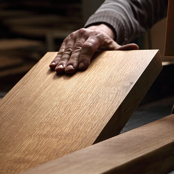 Main d’artisan posée sur une planche de chêne en atelier, photo d’ambiance pour la marque de menuiserie Atelier Orma