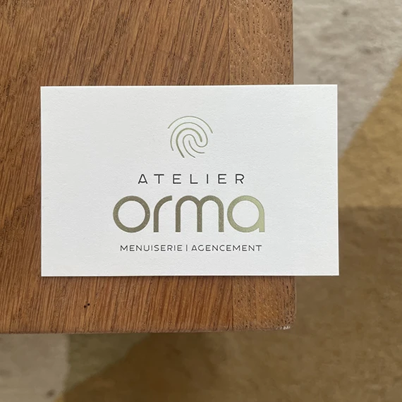 Carte de visite letterpress Atelier Orma posée sur une table en chêne, logo et empreinte en marquage à chaud vert
