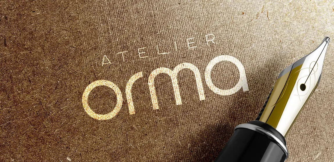 Logo Atelier Orma en lettrage clair sur papier kraft texturé, à côté de la plume d’un stylo noir et or