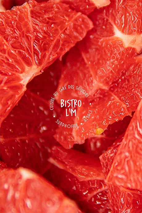 Logo circulaire Bistro L’M « Cuisine au gré des saisons, Sundhoffen, Alsace » sur un gros plan de pamplemousse rose