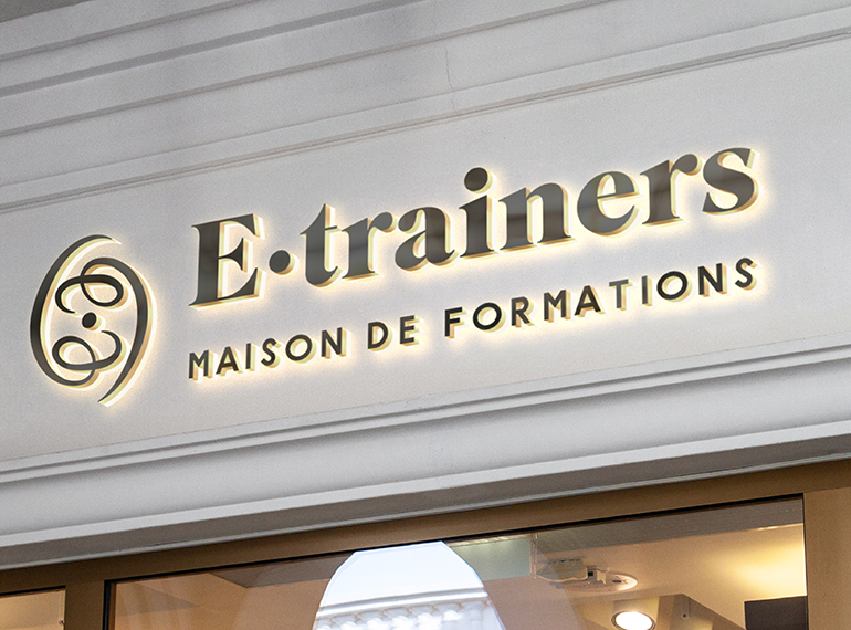 Enseigne E·trainers en lettres relief rétroéclairées au-dessus d’une vitrine, avec son emblème en arabesque