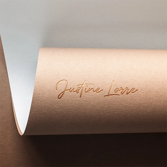 Signature Justine Lorre gravée en relief sur un papier rosé enroulé, déclinaison du logo de la coach