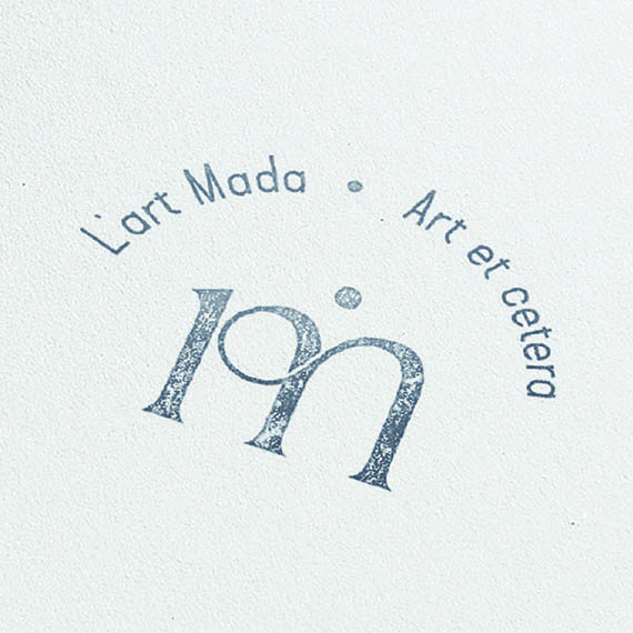 Tampon circulaire L’Art Mada à l’encre bleue sur papier blanc, monogramme lm entouré de « Art et cetera »