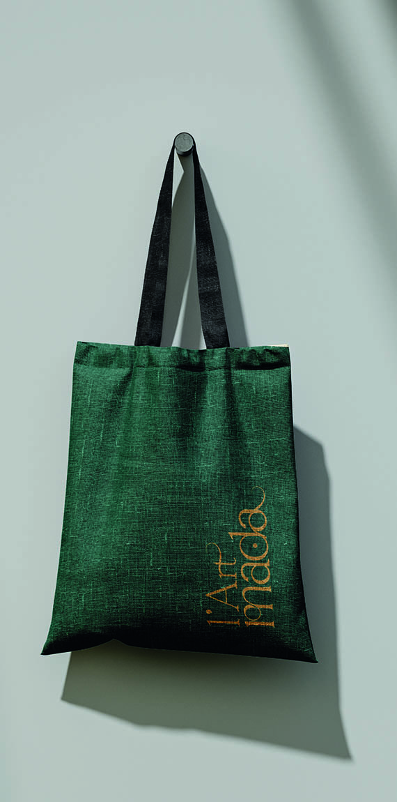 Tote bag en toile vert sapin suspendu à une patère, logo L’Art Mada imprimé en doré à la verticale