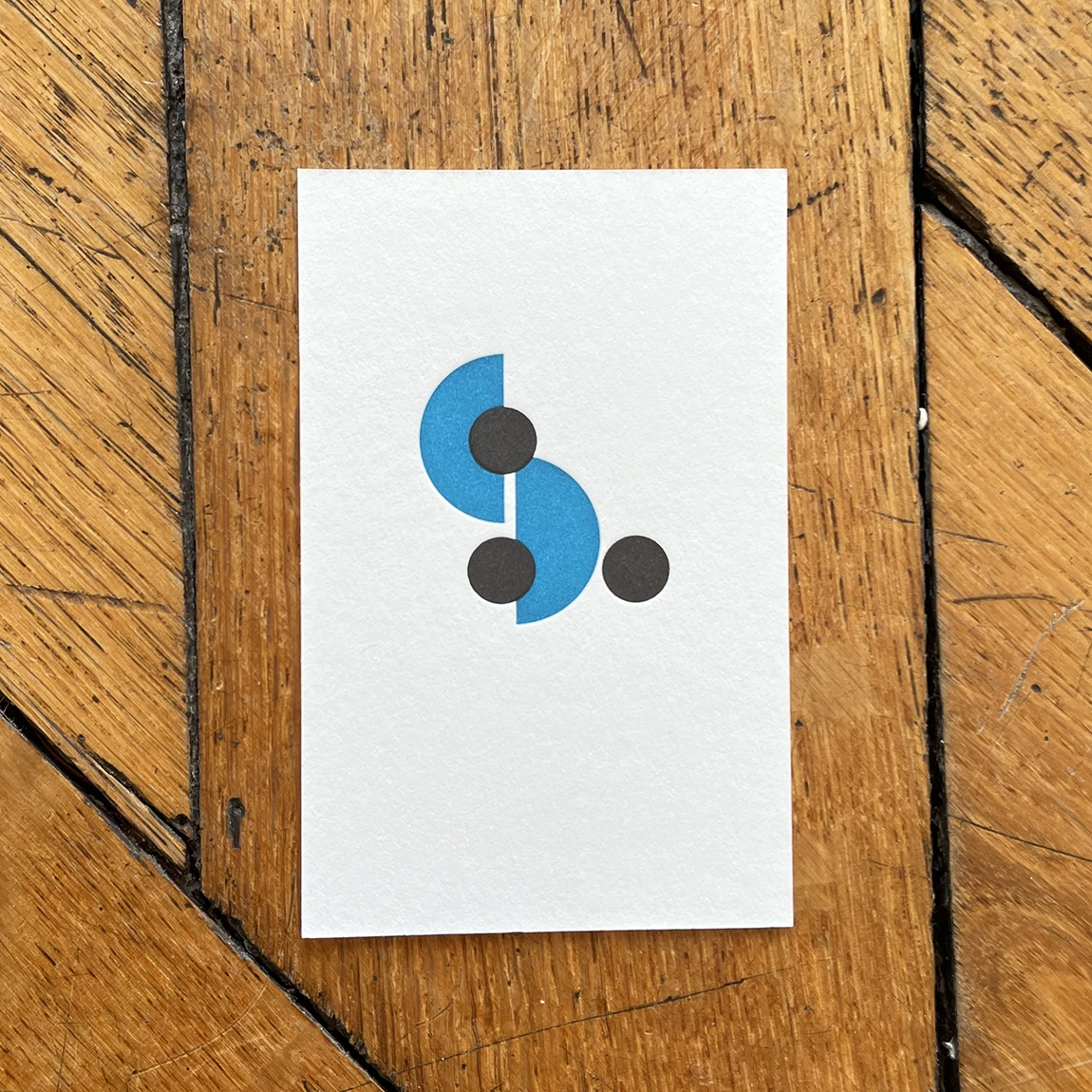 Carte imprimée en letterpress au logo bleu et noir de La femme assise, posée sur un parquet en chêne