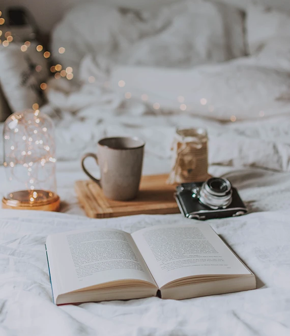 Livre ouvert, tasse et appareil photo argentique sur un lit blanc, planche d’ambiance du studio de design éditorial La femme assise