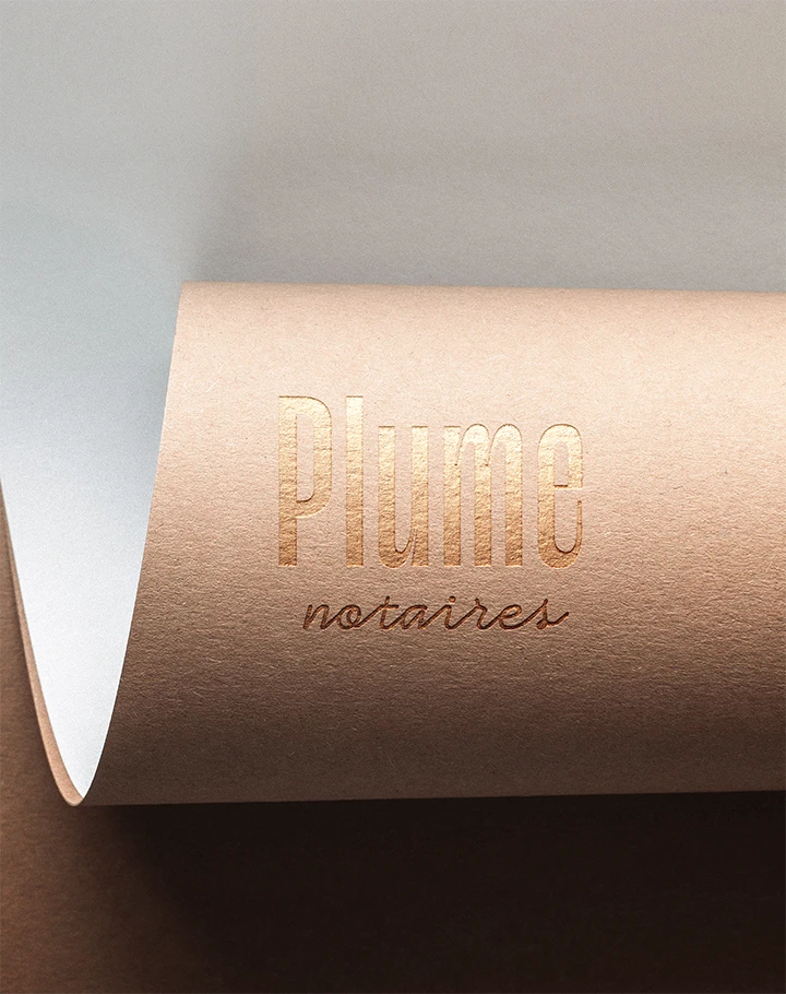 Logo Plume notaires en dorure cuivrée sur un papier kraft rosé enroulé, papeterie du cabinet notarial